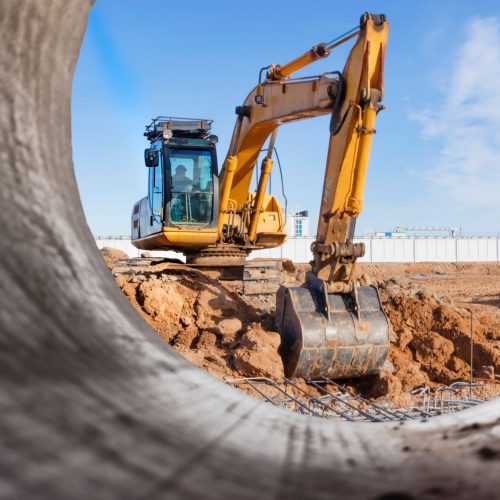View of a digger through a pipe on work site